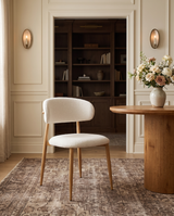 Bouclé Mabel Dining Chair with Oak-finish metal legs, three-quarter view beside a round fluted dining table